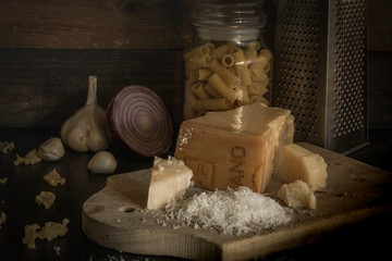 Parmesan cheese piece on wooden board. Grated Parmesan cheese with olive oil, garlic and pasta. The dark black background