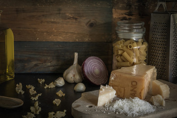 Parmesan cheese piece on wooden board. Grated Parmesan cheese with olive oil, garlic and pasta. The dark black background