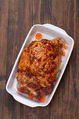 raw turkey leg with spices and vegetables on dish on wooden background
