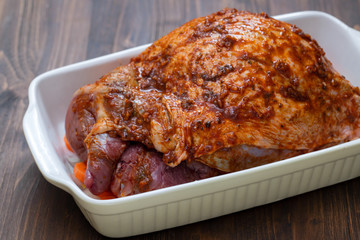 raw turkey leg with spices and vegetables on dish on wooden background