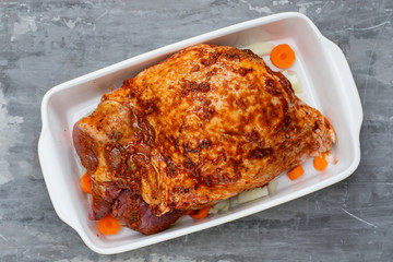raw turkey leg with spices and vegetables on dish on gray ceramic background