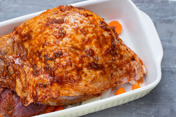 raw turkey leg with spices and vegetables on dish on ceramic background