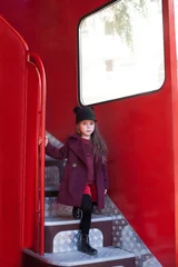 Foto op Plexiglas Little cheerful girl near the red English bus in a beautiful coat and a hat. Child's journey. School bus.  London red bus. Spring.  With the International Women's Day. Since March 8! © stock_studio