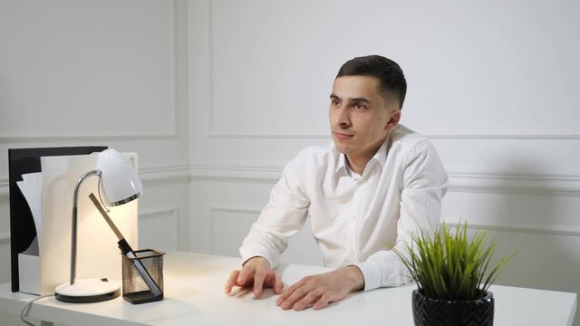 Office worker young man in white shirt is procrastinating sitting at work at the office table. Dreaming about something.