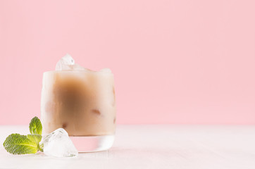 Irish coffee cocktail with cream and ice cube, green mint in misted glass on white wood board in light pink color background, copy space.
