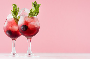 Exquisite red alcoholic shots of sweet berry liquor with ice cubes, blueberry, green mint on pastel soft light pink background.