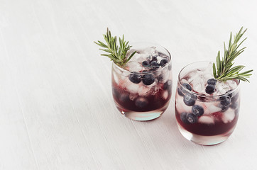 Fresh cold summer fruit cocktails with ice cubes, blueberry, rosemary on white wood board, top view.