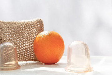 An orange is on the table and next to it are vacuum cans and a mesh washcloth made from natural fibers.