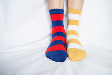 Women's legs in socks colors alternating, side stand on white fabric floor.