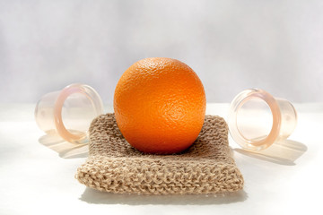 The orange lies on a mesh washcloth made from natural fibers, and next to it are vacuum banks.