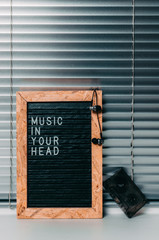 Letter board with the inscription music in your head in white letters on black.Headphones and audio cassette. Background of metal blinds.