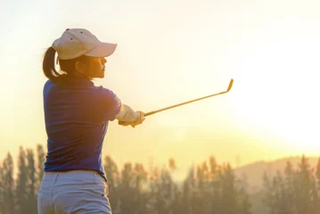 Selbstklebende Fototapeten Healthy Sport. Asian Sporty woman golfer player doing golf swing tee off on the green evening time, she presumably does exercise.  Healthy Lifestyle Concept. © freebird7977