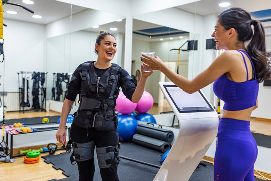 Young woman fitness instructor works with woman wearing ems equipment as she exercises in a studio. Smiling satisfied female coach training woman