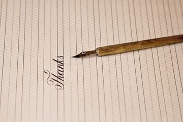 word thanks is written with a wooden ink pen on a white paper sheet with stripes drawn. stationery...