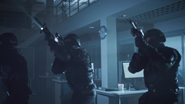 Masked Team of Armed SWAT Police Officers Slowly Move in a Hall of a Dark Seized Office Building with Desks and Computers. Soldiers with Rifles and Flashlights Surveil and Cover Surroundings.