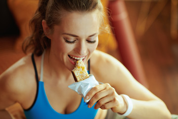 happy active woman in modern house biting fitness energy bar