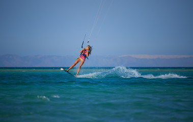 Kite surfing girl in sexy swimsuit with kite in sky on board in blue sea riding waves with water...