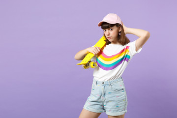 Portrait of beautiful teen girl in vivid clothes looking camera holding yellow skateboard isolated on violet pastel background in studio. People sincere emotions lifestyle concept. Mock up copy space.