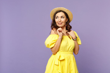 Pretty pensive cute young woman in yellow dress, summer hat standing, looking aside isolated on pastel violet wall background in studio. People sincere emotions, lifestyle concept. Mock up copy space.