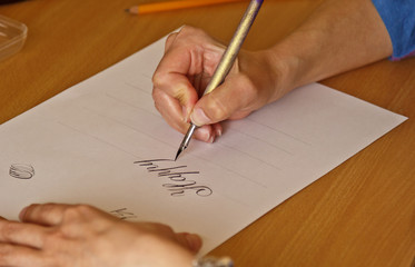 female hand writes word happy with the inky pen on a white paper sheet with stripes. stationery on desk close up top view. spelling lessons and caligraphy exercises. Template, layout, background