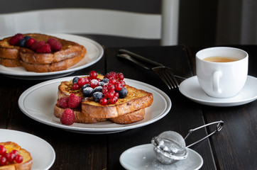 Fresh french toasts with fruit and cup of coffee on wooden table in restaurant. Good breakfast background.