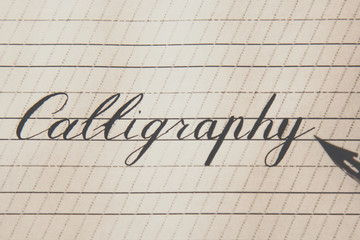 word calligraphy is written with an ink pen on a white paper sheet with stripes drawn. stationery close up top view. spelling lessons and caligraphy exercises. Template, layout, background. macro
