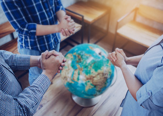 Three people standing and pray to God for the world with blurred world globe on wooden table,...
