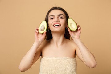 Close up brunette half naked woman 20s with perfect skin nude make up hold avocado isolated on beige pastel wall background studio portrait. Healthcare cosmetic procedures concept. Mock up copy space.