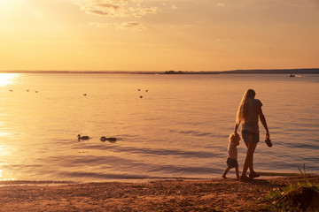 Young mother plays with her child in the summer near the lake at sunset in the evening
