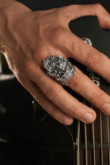 Cropped closeup shot of man's hand, touching the headstock of a guitar. The guy is wearing massive...