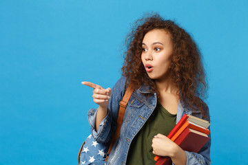 Young african american girl teen student in denim clothes, backpack hold books isolated on blue wall background studio portrait. Education in high school university college concept. Mock up copy space