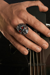 Cropped closeup shot of man's hand, touching headstock of guitar. The guy is wearing seal-ring in...