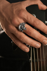 Cropped closeup shot of man's hand, touching headstock of guitar. The guy is wearing massive ring...