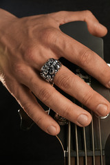Cropped closeup shot of man's hand, touching headstock of guitar. The guy is wearing massive ring...