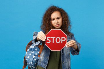 Young african american girl teen student in denim clothes, backpack hold stop isolated on blue wall...