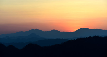 sun setting behind a dense forest area followed by mountains.