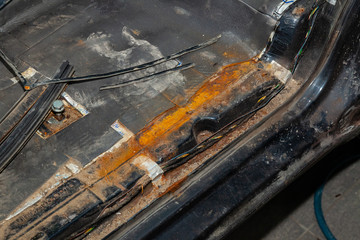 The threshold and the floor of the car with bright red rust and corrosion in the back of a black...