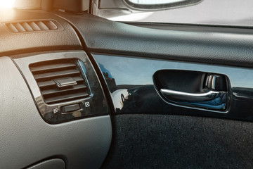 A close-up view of a part of the interior of a modern luxury car with a view of a silver-colored door handle on a chrome finish with black wood trim after dry cleaning. Auto service industry.