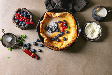 Fresh baked Dutch baby pancake in iron cast pan served with blackberry and red currant berries,...