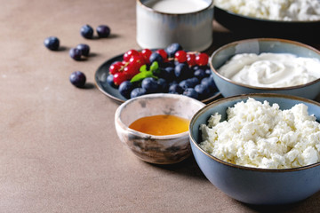 Dairy produce for breakfast. Cottage cheese, plain yogurt, milk, cream, honey, blueberries and red currant berry in ceramic bowl over brown table. Healthy eating. Copy space