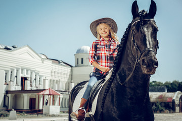 Obraz premium Joyful cute blonde girl sitting on a horse