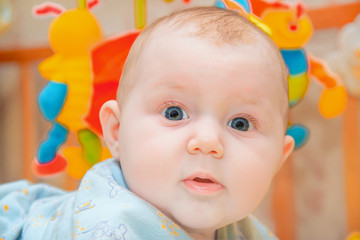 A newborn baby is lying in a children's bed on the background of toys and smiling, close-up.