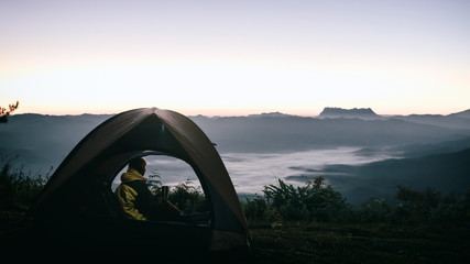 Tourist with holding coffee cup sitting in the tent around mountains under sunrise light sky enjoying the leisure and freedom.