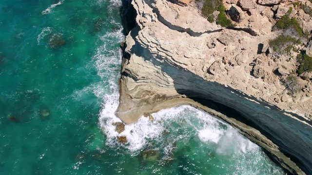 Strong waves break on rocky seashore on sunny day, view from above
