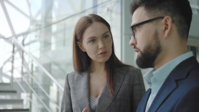 Beautiful young successful business woman in a suit communicates with a colleague or partner while standing in a bright high-tech business center against the background of the stairs.