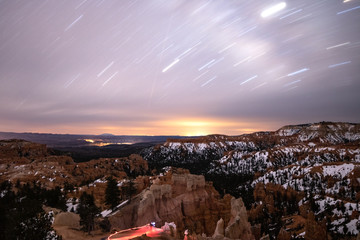 Star trails streaking across the night sky over a snow covered desert landscape. Bryce Canyon...