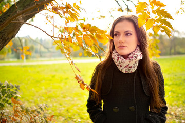 Beautiful romantic girl with perfect skin in autumn park, enjoying the perfect weather in a sunny day. Gorgeous young woman outdoors. Close-up shot in natural light, retouched, vibrant colors
