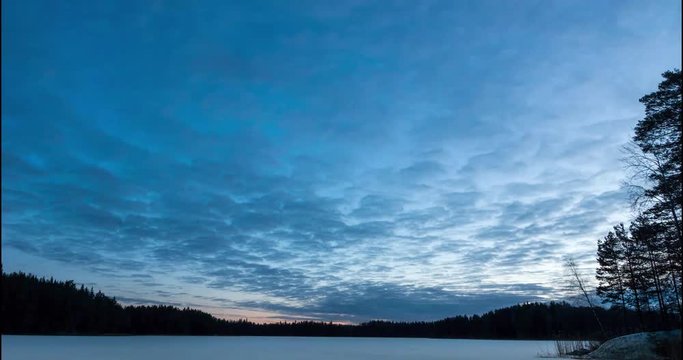 Timelaps of clouds moving over frozen lake before sunrise