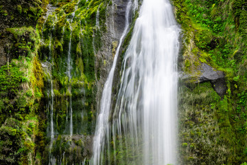 Small waterfall by Seljalandsfoss, Iceland with closeup of long exposure smooth blurred white water falling off cliff in green mossy summer rocky landscape