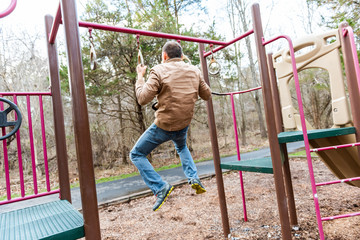 Obraz premium Young fit man exercising doing chin pull ups on bar in playground park in autumn winter or spring calisthenics